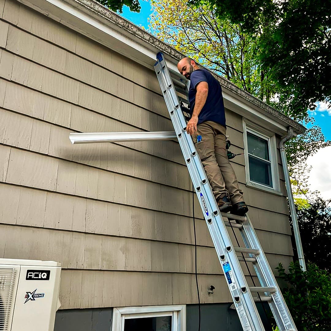 An EcoSave technician on a ladder inspecting the eaves of a home