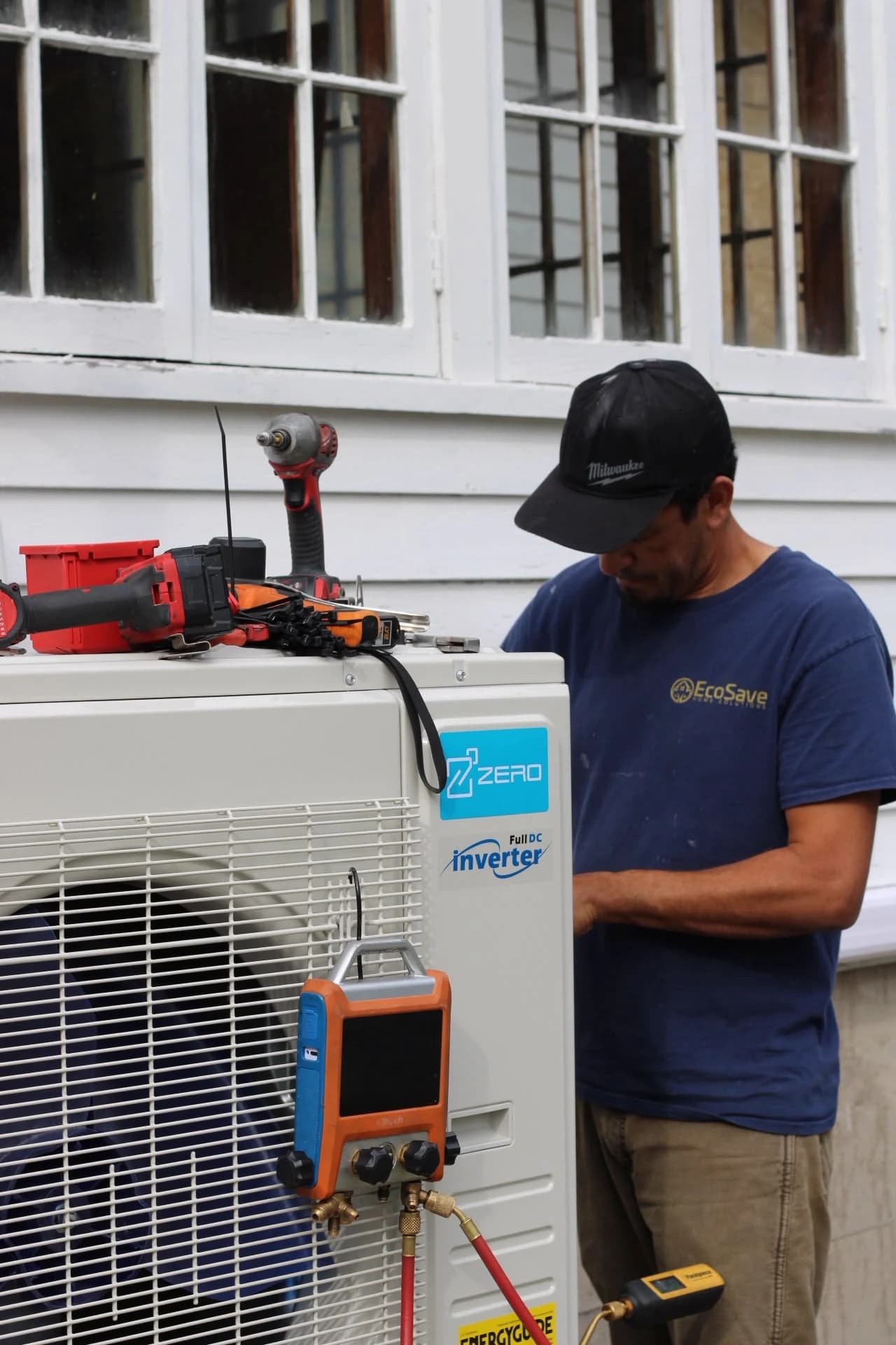 EcoSave technician working beside an outdoor heat pump with tools and gauges